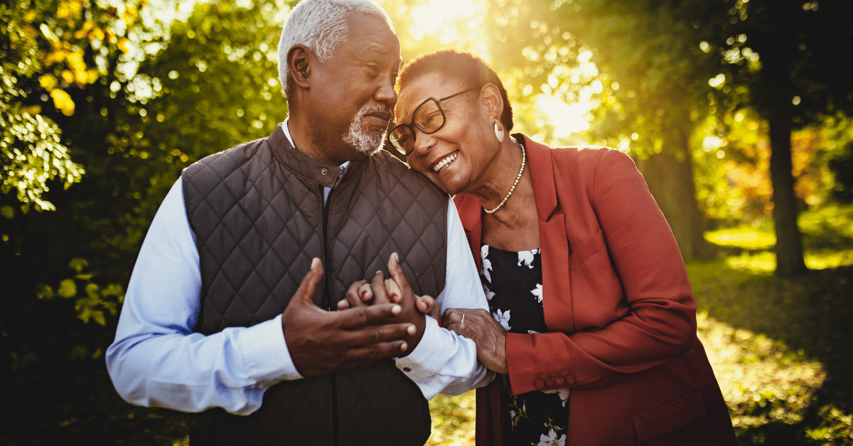 senior couple (husband and wife) holding hands with head on shoulder and sun streaming