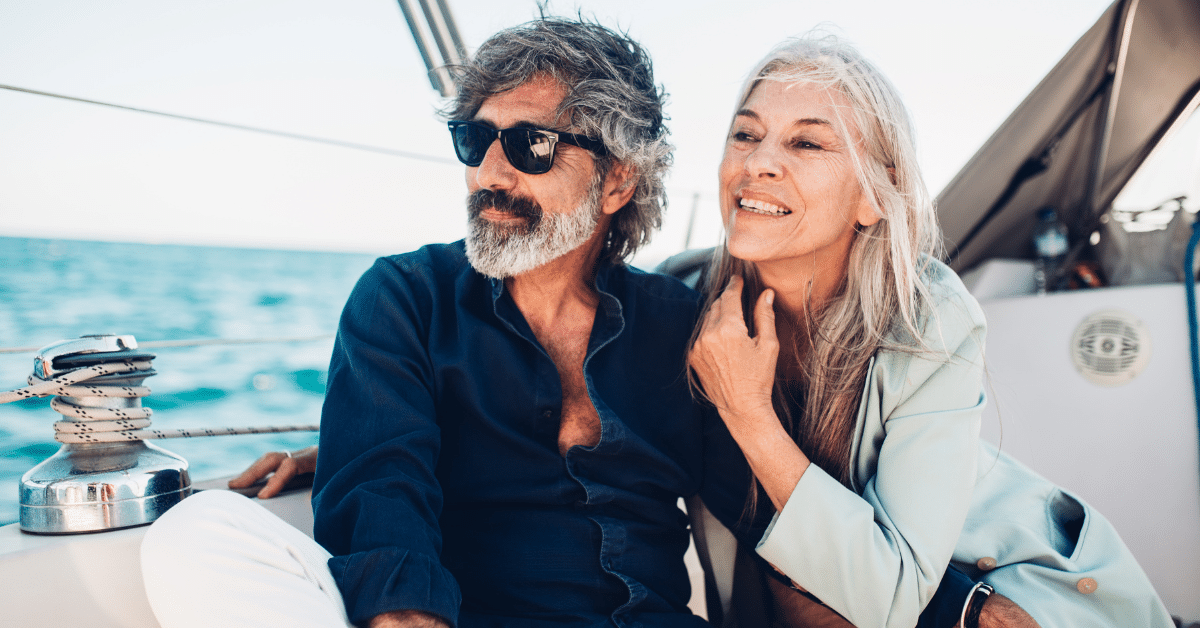 68 couple sitting on a sailboat with the ocean behind them.