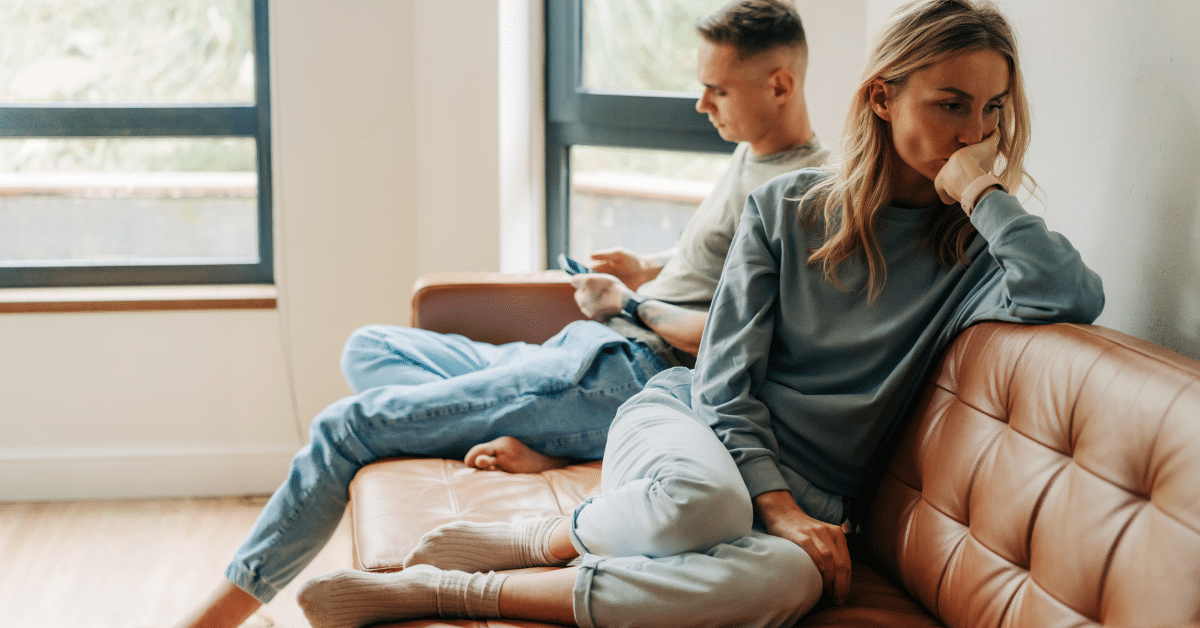 man and woman sitting on a couch. Man is on his phone and woman is looking away as if they are arguing
